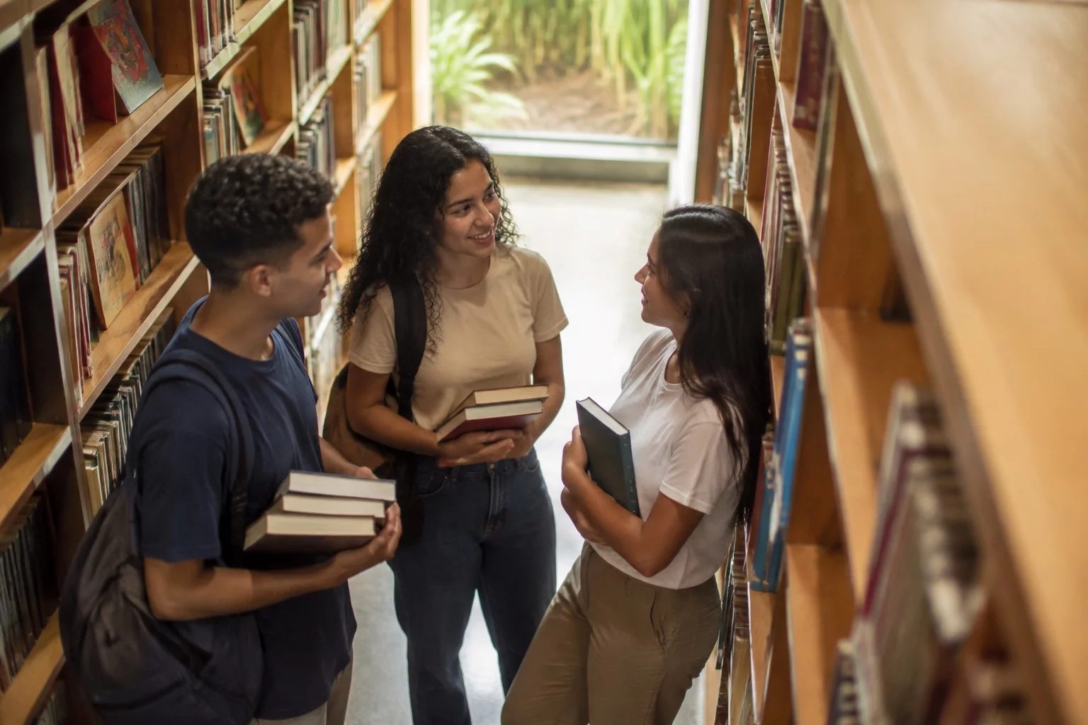 Estudantes conversando em pé entre as estantes de uma biblioteca