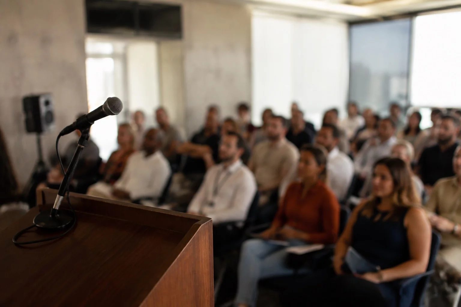 Microfone sobre uma tribuna, com a plateia sentada desfocada ao fundo
